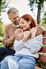 A loving couple dressed casually, sitting together on a wooden bench in a serene park setting.