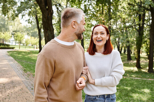 A man and a woman in casual attire stroll through a lush park.