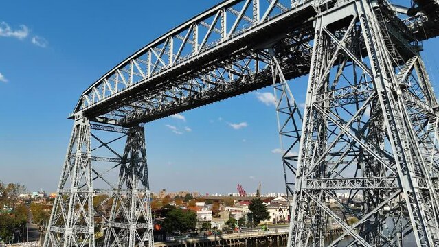 Ferry bridge on the riachuelo and panoramic view of La Boca neighborhood in Buenos Aires, Argentina. Aerial camera passes under the bridge and moves over the water showing the city