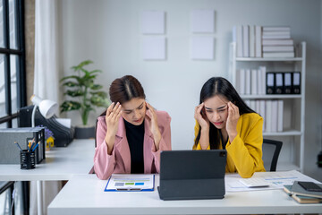 Two women are sitting at a desk with a laptop and papers in front of them