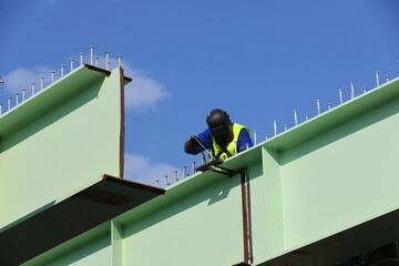 A worker use a welding machine to weld a large and heavy metal section of a bridge under construction.