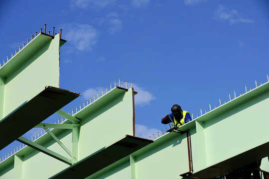 A worker use a welding machine to weld a large and heavy metal section of a bridge under construction.
