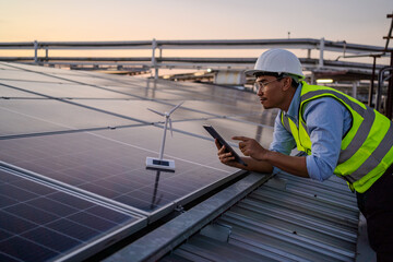A man in a yellow vest is looking at a tablet while standing on a solar panel. He is pointing at something on the tablet