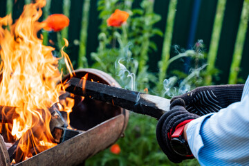 In an outdoor setting, a skilled blacksmith is seen shaping and molding metal using gloves and tongs over open fire, displaying traditional craftsmanship techniques