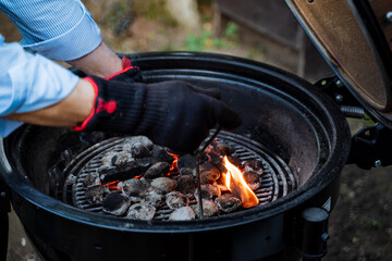 A man is safely lighting charcoal on a grill for an outdoor BBQ preparation, wearing safety gloves....