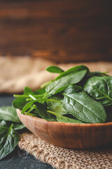 Fresh organic spinach leaves in a wooden bowl over dark rustic background. Top view with copy space