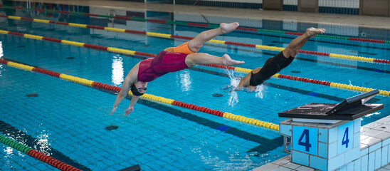 Two female swimmers taking the start and jumping in a pool