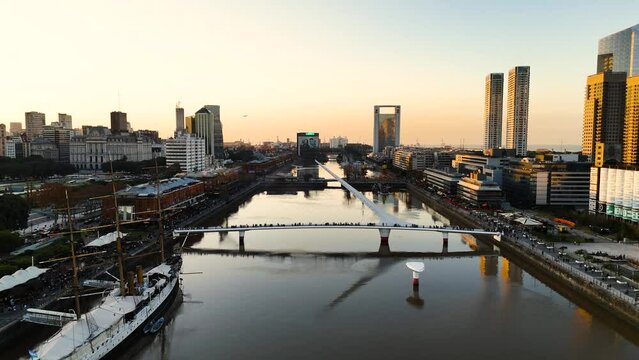 Buenos Aires, Argentina - June 1, 2024: Women's Bridge full of tourists in Puerto Madero district during the golden hour. Aerial camera over the water flies over the bridge with sun backlight