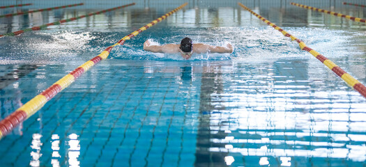 Male professional athlete swimming in butterfly style, with both arms moving symmetrically, making water splash