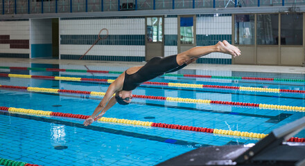 Professional female swimmer preparing and jumping off the starting block into the pool. Competitive...