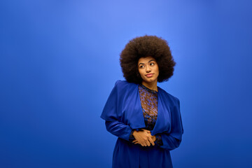 A stylish African American woman with curly hairdohairstyle standing against a vibrant blue...