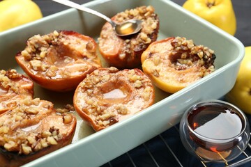 Tasty baked quinces with nuts and honey in dish on grid, closeup