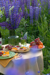 Brunch picnic with sweets and wine in spring blossom garden on a beige tablecloth on a sunny day, violet blossoms. Outdoor spring mood