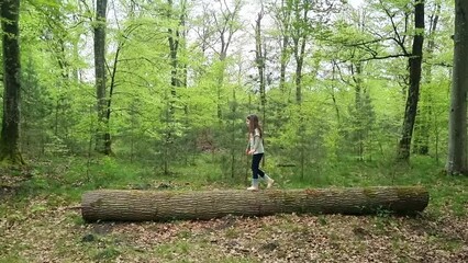 Little girl climbing broken tree like a bridge in a wooden area. High quality FullHD footage