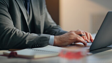 Closeup man hands typing laptop keyboard taking notes writing at office desk