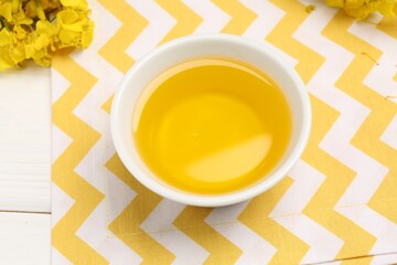 Rapeseed oil in bowl and beautiful yellow flowers on white wooden table