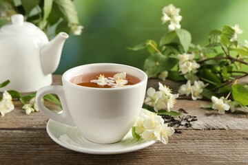 Aromatic jasmine tea in cup, flowers, green leaves and teapot on wooden table outdoors