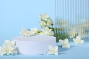 Presentation of product. White podium and beautiful jasmine flowers on light blue background, closeup