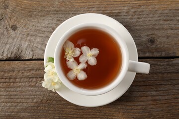Aromatic jasmine tea in cup and flowers on wooden table, top view