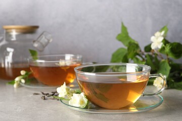 Aromatic jasmine tea in cups, flowers and green leaves on light grey table