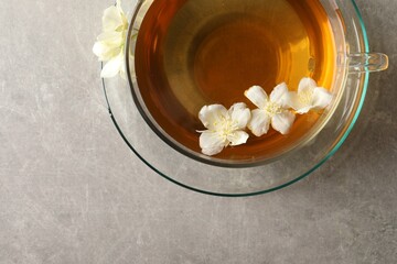 Aromatic jasmine tea in cup and flowers on light grey table, top view