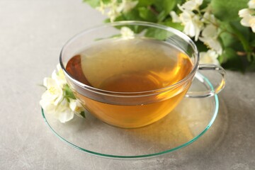 Aromatic jasmine tea in cup, flowers and green leaves on light grey table, closeup