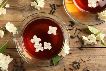 Hot jasmine tea in cups and flowers on wooden table, flat lay