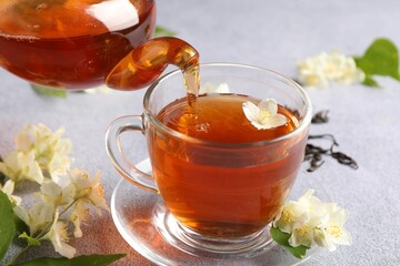 Pouring hot jasmine tea into cup on light grey table, closeup