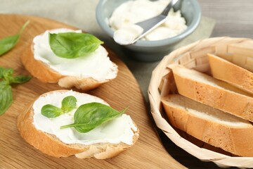 Delicious sandwiches with cream cheese and basil leaves on wooden table, closeup