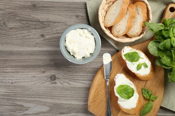 Delicious sandwiches with cream cheese and basil leaves on wooden table, flat lay. Space for text