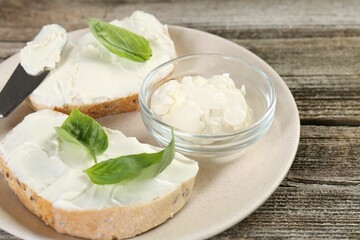 Delicious sandwiches with cream cheese and basil leaves on wooden table, closeup