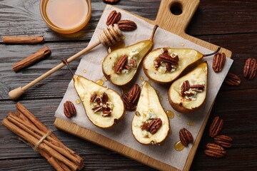 Tasty baked pears with nuts, blue cheese, thyme, honey and cinnamon sticks on wooden table, flat lay