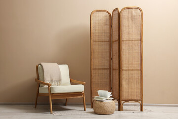 Folding screen, armchair and blanket near beige wall indoors