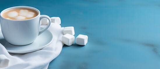 Cup of coffee topped with marshmallows on a saucer, placed on a blue linen cloth. with copy space image. Place for adding text or design