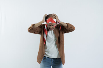 Asian man holding cell phone and showing gesture of disappointment expression. Bald-headed Asian man wearing a headband typical of the independence day of the republic of indonesia