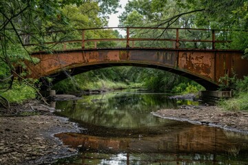 Weathered iron bridge arching over a calm forest stream surrounded by lush greenery