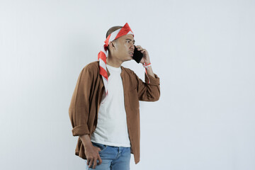 Asian man on the phone with an angry expression. Bald-headed Asian man wearing a headband typical of the independence day of the republic of indonesia