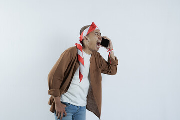 Asian man on the phone with an angry expression. Bald-headed Asian man wearing a headband typical of the independence day of the republic of indonesia