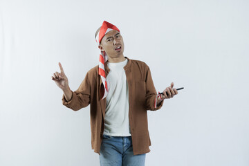 Asian man holding cell phone and showing gesture of disappointment expression. Bald-headed Asian man wearing a headband typical of the independence day of the republic of indonesia
