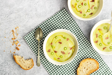Bowls with green asparagus soup and toasted bread on gray cement background.