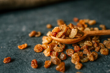 Raisins in a wooden spoon scattered on a black background