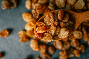 Raisins in a wooden spoon scattered on a black background