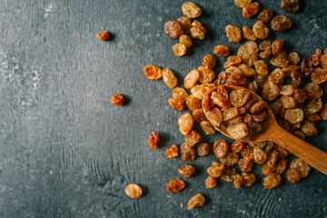 Raisins in a wooden spoon scattered on a black background