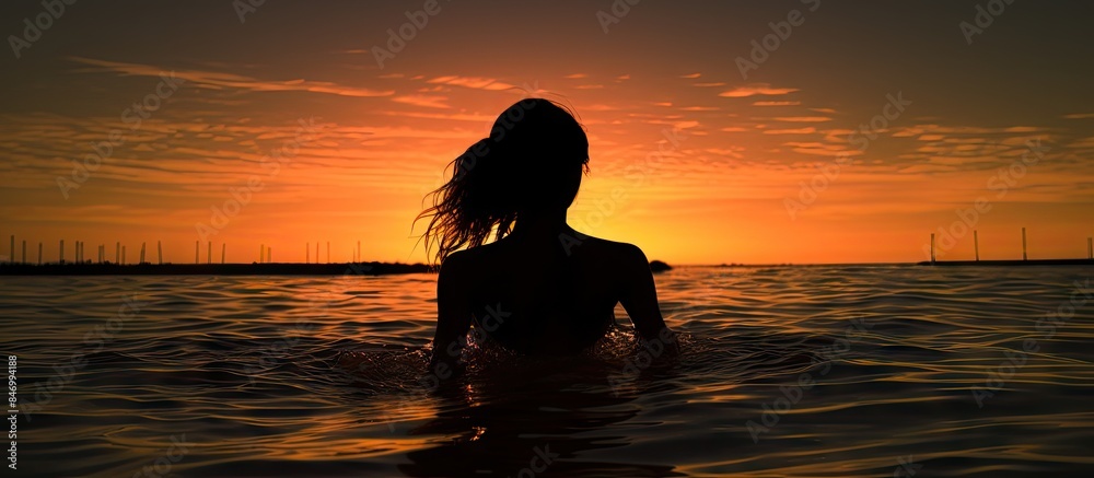 Leinwandbilder silhouette of a woman wading in the water under the colorful hues of a sunset sky in a horizontal co