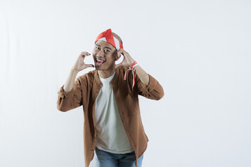 Asian man with Indonesian flag headband forming love symbol, celebrating Indonesia's independence day August 17, independence day concept, isolated white background.