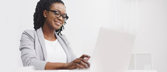 An office employee black lady is focused on her computer at her desk. The atmosphere is professional and modern, with a clean desk and bright space, highlighting concentration.