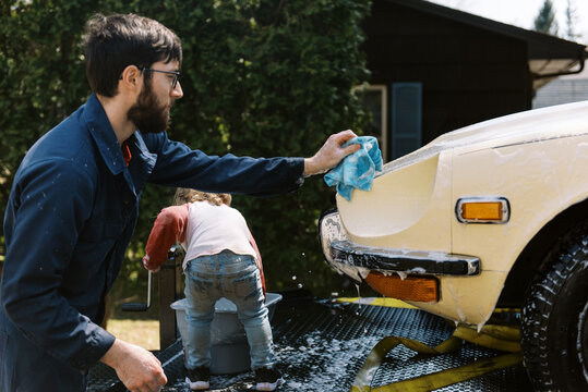 toddler girl and her father washing car in driveway together