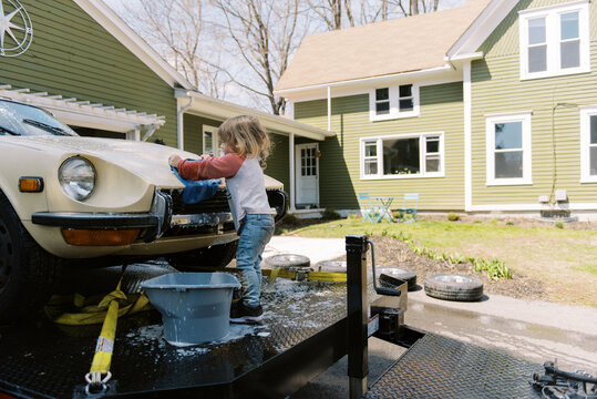 toddler girl washing classic car outdoors with soap and cloth