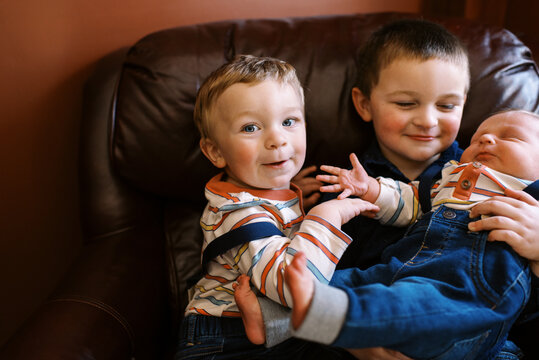 toddler brothers holding their newborn brother while on couch