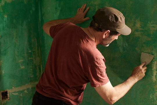 Handyman at work with spatule removing old wall paper in a room